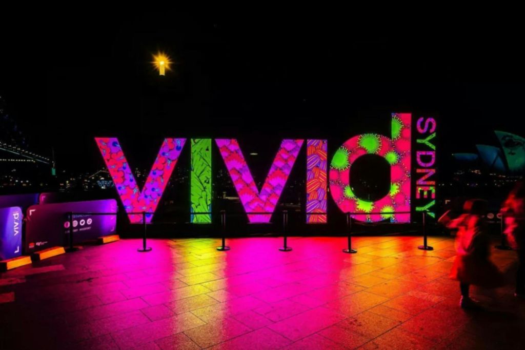 어두운 배경을 배경으로 밤에는 선명한 색상과 패턴으로 '비비드 시드니 (Vivid Sydney)' 표지판을 비춥니다.