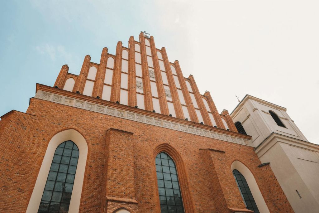 높은 아치형 창문과 수직 버팀대가 있는 고딕 양식의 벽돌 교회 정면을 낮은 각도에서 바라볼 수 있습니다.