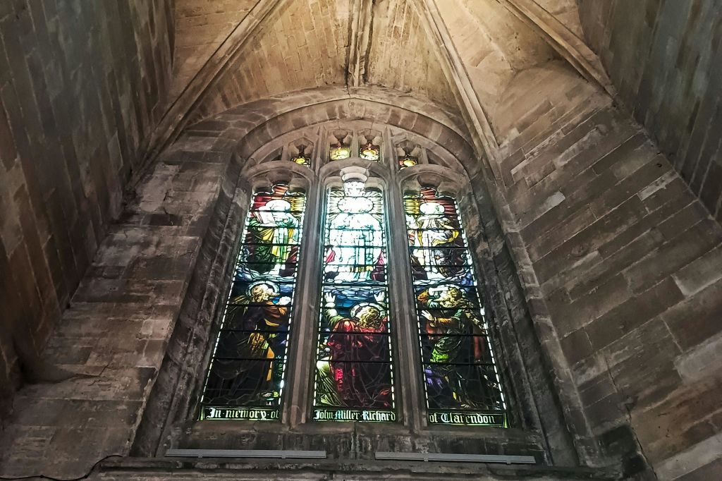 석조 고딕 양식의 아치에 세워진 교회의 커다란 스테인드글라스 창문은 다채로운 종교적 장면을 묘사하고 있습니다.