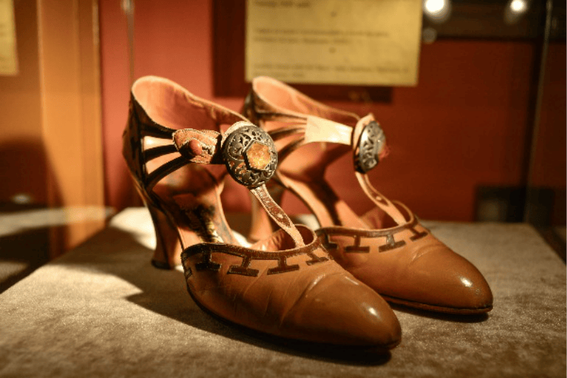 정교한 스트랩과 화려한 버클이 달린 빈티지 브라운 가죽 힐이 부드러운 표면에 전시되어 있습니다.