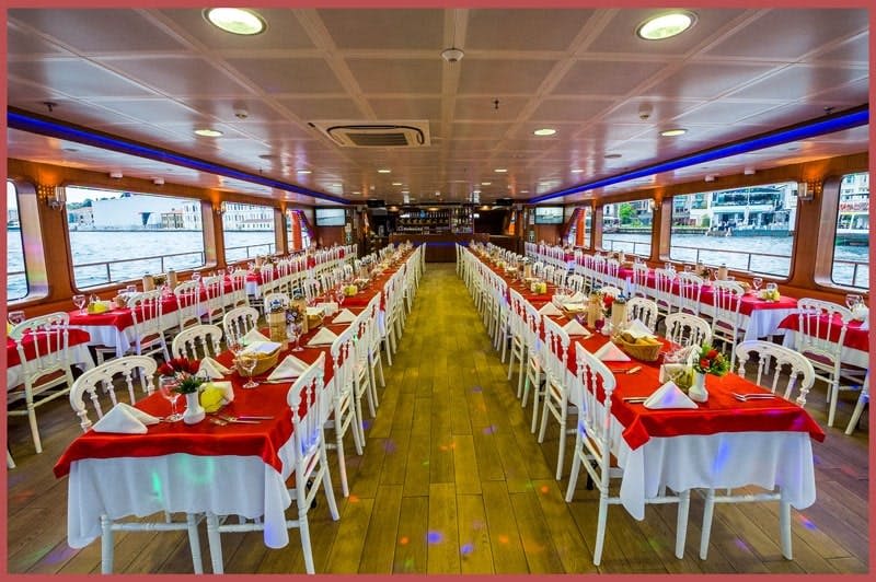 빨간색과 흰색 테이블이 있는 보트의 넓고 우아한 식사 공간으로, 양쪽 창문이 길게 나란히 배치되어 있습니다.