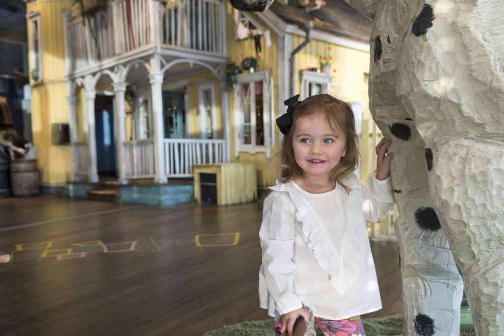 흰색 상의를 입은 어린 소녀가 검은 반점이 있는 크고 하얀 조각상 옆에 서서 나무 바닥이 있는 밝게 빛나는 방 안에서 미소를 짓고 있습니다.