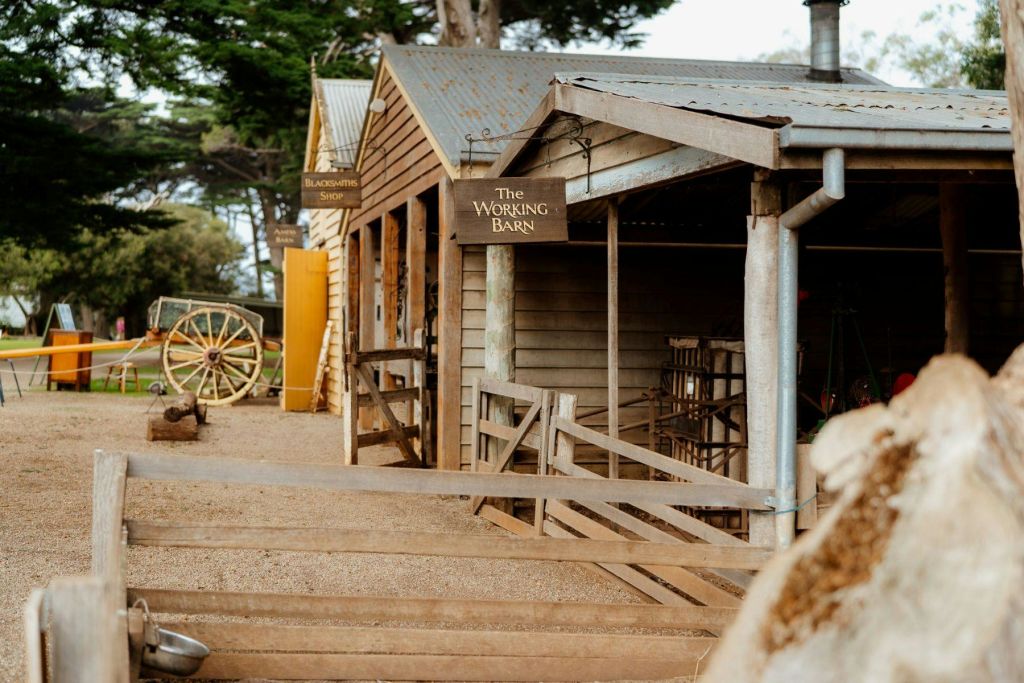 "대장장이 가게" 옆에 "일하는 헛간" 이라고 적힌 팻말이 있는 나무 헛간. 근처에는 나무 마차 바퀴와 펜싱이 있습니다.
