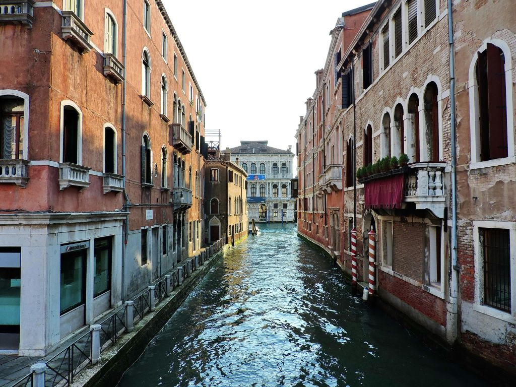 양쪽에 유서 깊은 건물이 있는 좁은 운하로, 잔잔한 물이 구조물을 반사합니다.