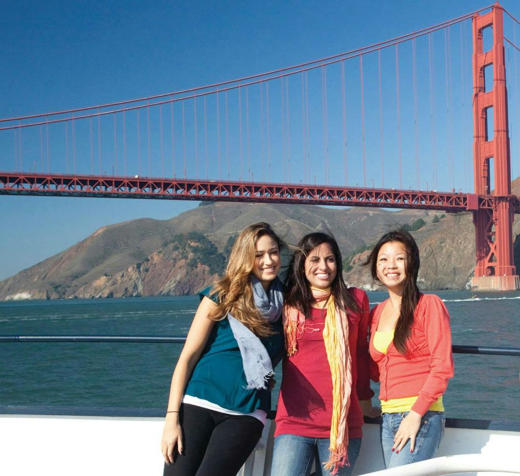 맑고 푸른 하늘과 언덕 풍경을 배경으로 금문교 앞에서 미소 짓는 세 명의 여성.
