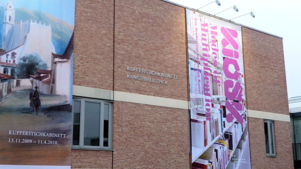 "Kupferstichkabinett Kunstbibliothek" 이라는 문구가 표시된 벽돌 외관과 대형 수직 배너가 있는 건물.