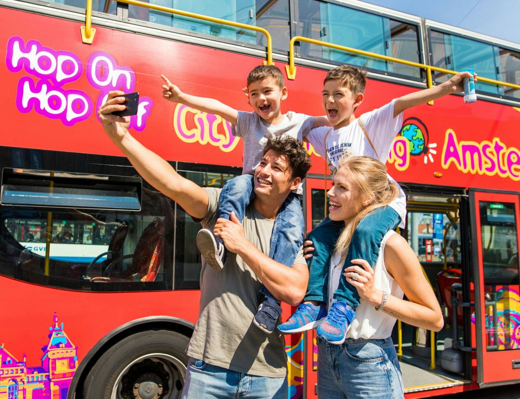 4인 가족이 빨간색 2층 투어 버스 앞에서 셀카를 찍고 있습니다.