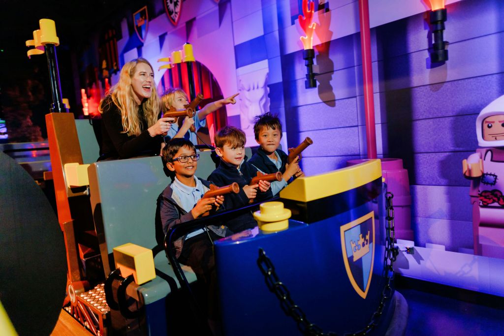 한 여성과 세 명의 소년이 장난감 총을 들고 화려한 중세 테마의 배경으로 미소를 지으며 라이딩을 즐깁니다.