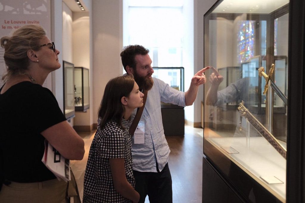 세 사람이 박물관에서 전시회를 관람하고, 한 명은 가리키며 설명하고, 다른 한 명은 주의 깊게 경청합니다.