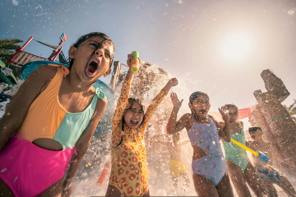 형형색색의 수영복을 입은 아이들이 햇살 가득한 워터파크에서 물놀이를 즐깁니다.