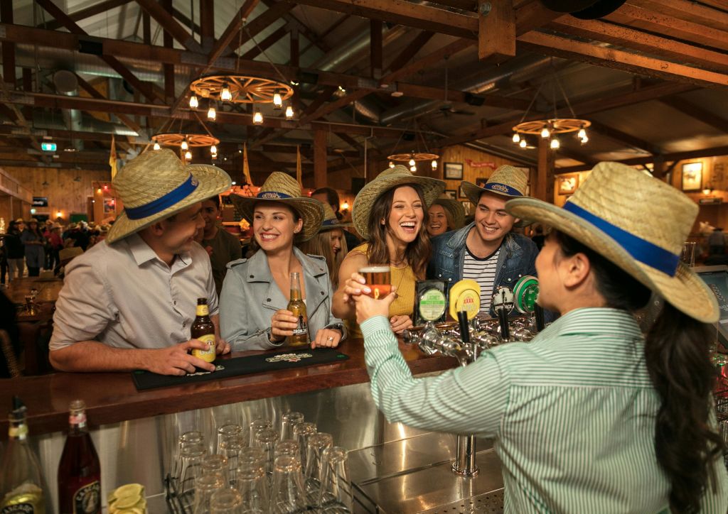 밀짚 모자를 쓰고 바에서 음료를 마시며 웃고 어울리는 사람들. 바에는 여러 개의 맥주 탭과 행잉 라이트가 있습니다.