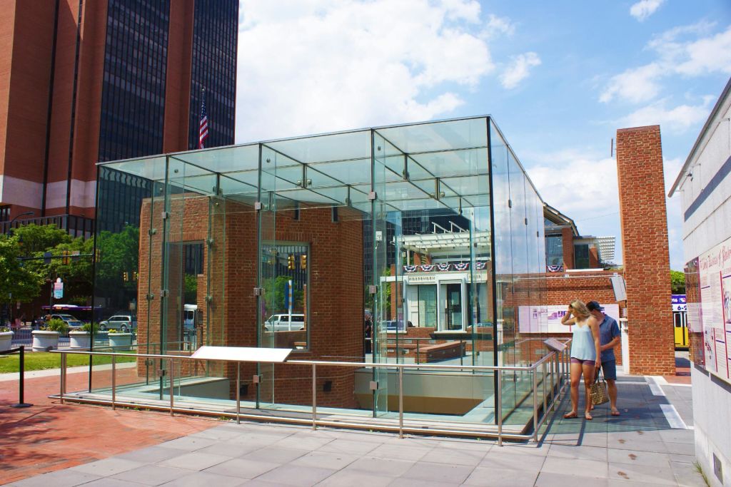 내부에 벽돌 벽이 있는 유리로 둘러싸인 구조물과 안내 패널, 두 사람이 대형 야외 디스플레이를 바라보고 있습니다.