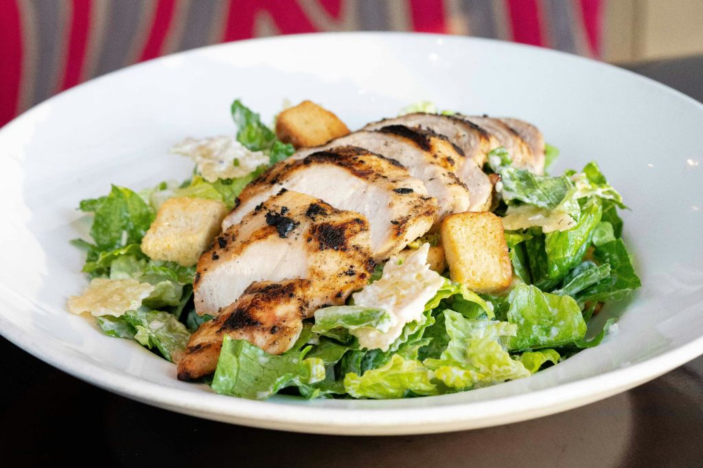 시저 샐러드 침대에 구운 치킨 슬라이스, 흰색 그릇에 크루통이 담겨 있습니다.