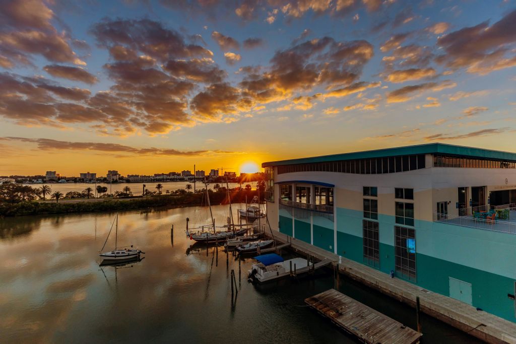 현대적인 건물에 정박한 요트, 잔잔한 물, 하늘에 흩어져 있는 구름이 있는 정박지 위로 석양을 감상해보세요.