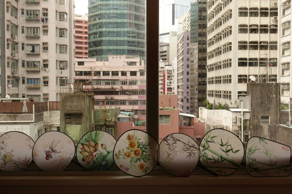 높은 건물의 도시 경관이 내려다보이는 창턱에는 꽃과 대나무 디자인의 장식용 선풍기가 놓여 있습니다.