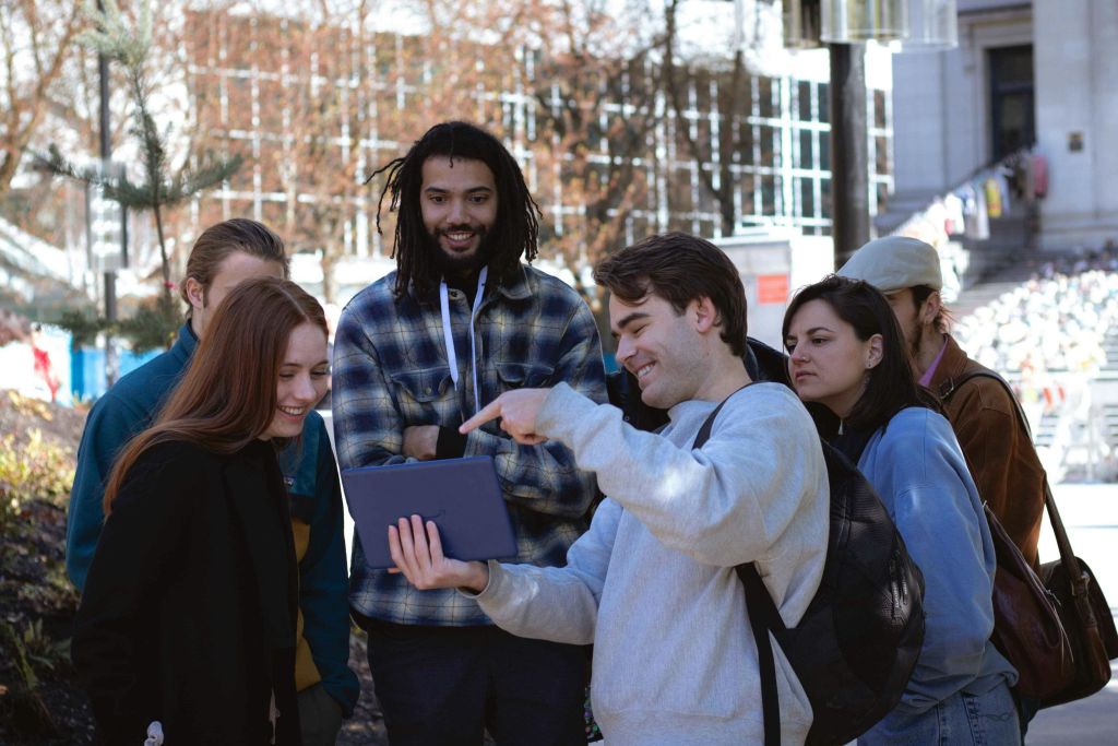야외에서 태블릿을 바라보는 한 무리의 사람들이 미소를 지으며 한 사람이 화면을 가리키고 있습니다.