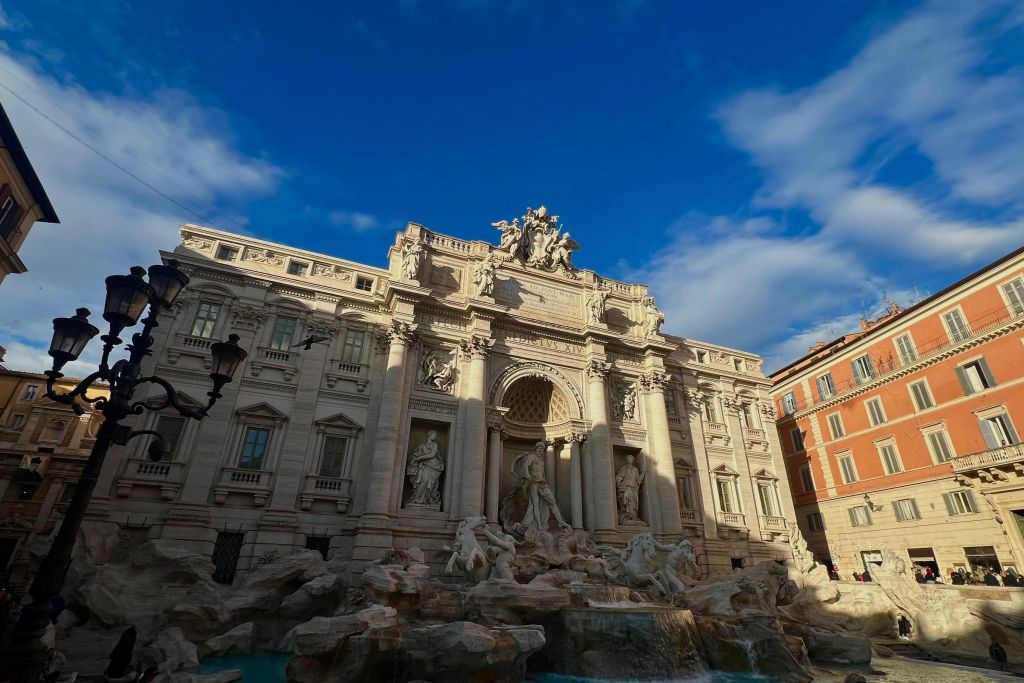 화려한 건물로 둘러싸인 푸른 하늘 아래 도시 광장에 조각품이 있는 바로크 양식의 분수.