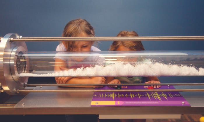 두 명의 어린이가 탁상 디스플레이 패널의 투명 실린더 내부에서 폼 패턴을 관찰합니다.