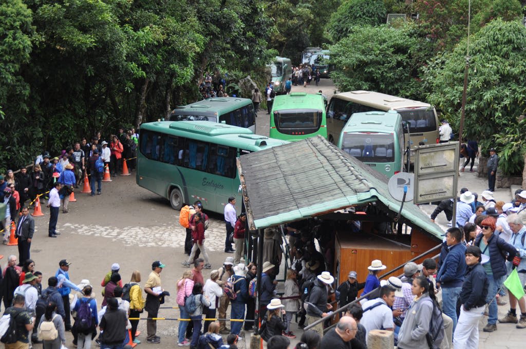 녹음이 우거진 좁은 골목에 있는 녹색 버스 근처에서 줄을 서는 사람들로 가득합니다.