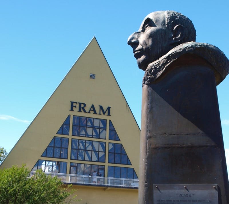 커다란 창문과 전경에 남성의 흉상이 있는 "프램" 이라고 표시된 삼각형의 노란색 건물.