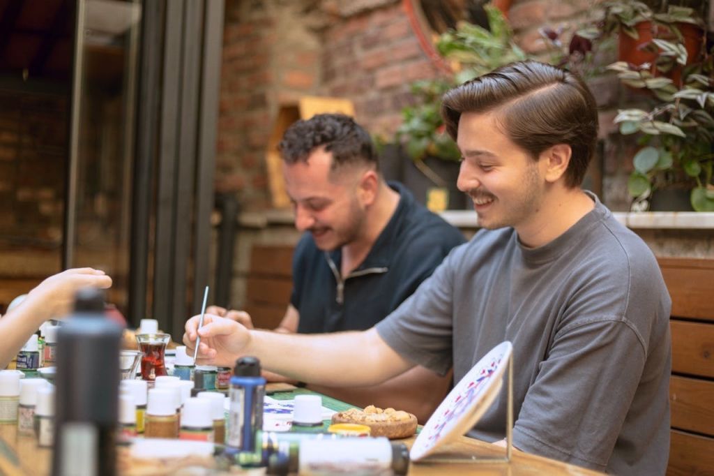 식탁에 앉아 미소를 짓고 있는 두 사람. 전경에 미술 용품과 장식 접시가 놓여 있습니다.