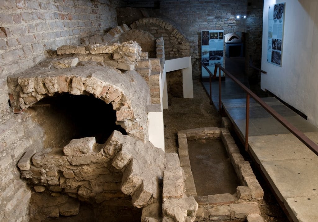 석조 아치와 통로, 정보 표시판, 주변 조명이 있는 고대 지하 유적.