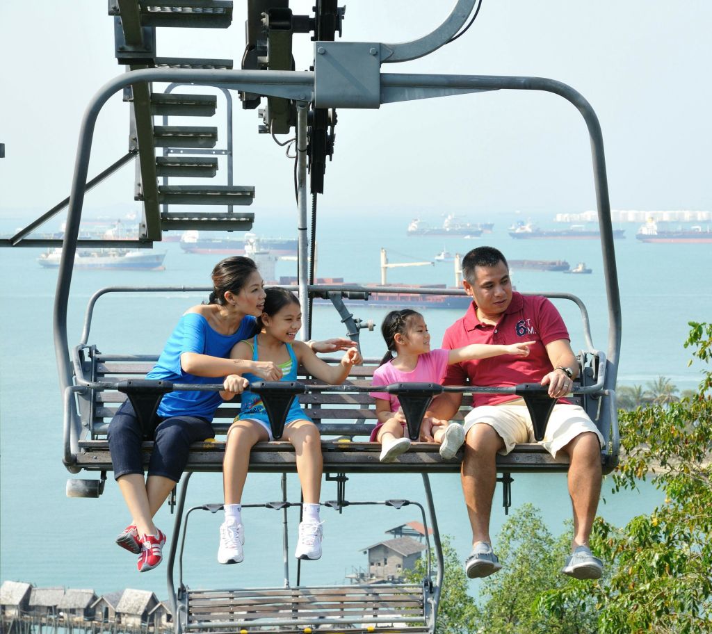 4명의 가족이 의자 리프트에 앉아 선박과 먼 해안선이 있는 바다의 아름다운 전망을 즐기고 있습니다.