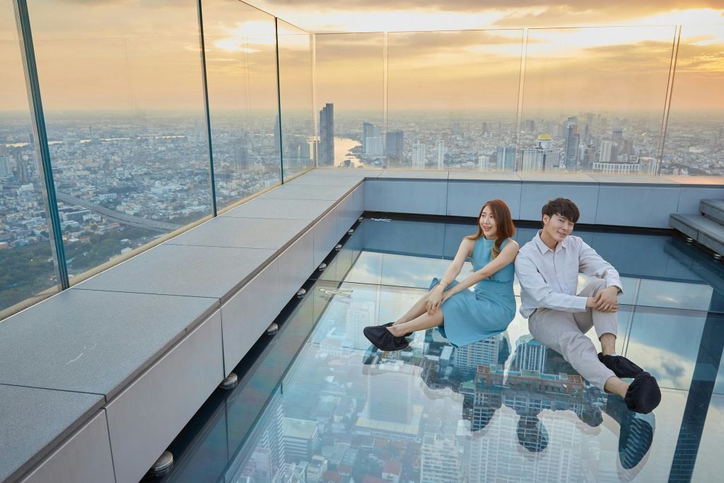 해가 질 무렵 한 남녀가 옥상의 유리 바닥에 앉아 도시 풍경이 내려다보입니다.