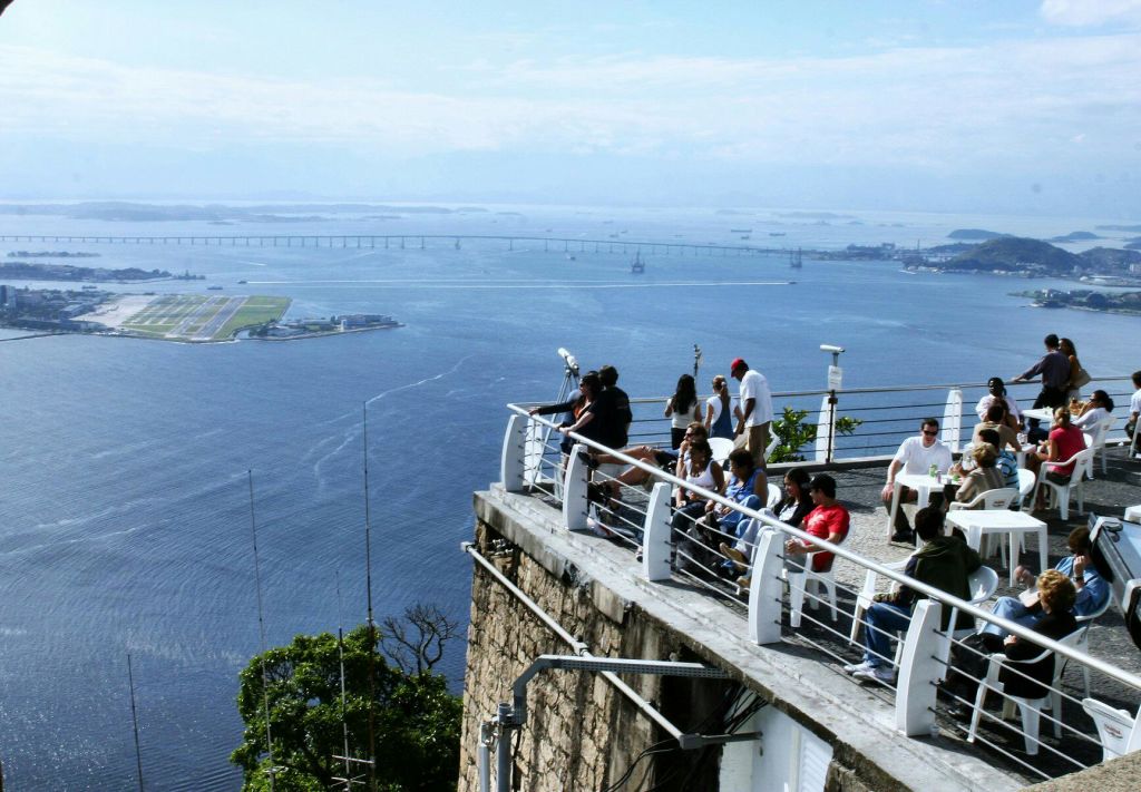 멀리 떨어진 다리와 작은 녹지로 가득 찬 섬이 있는 커다란 물줄기가 내려다보이는 전망대 위의 사람들.