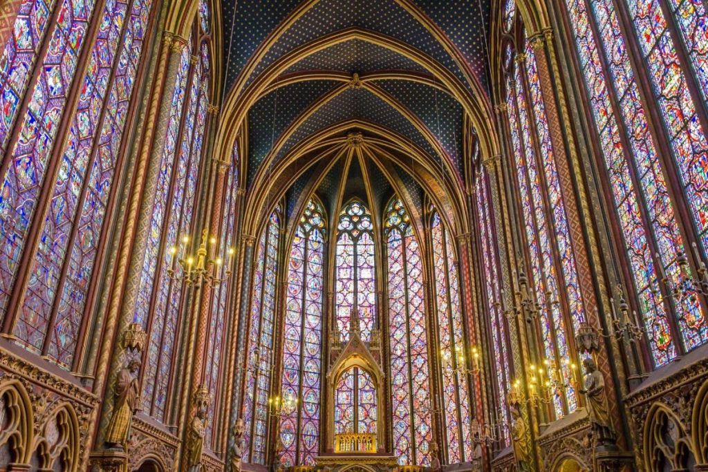 높은 스테인드글라스 창문, 뾰족한 아치, 화려한 샹들리에가 있는 고딕 양식의 대성당 내부.