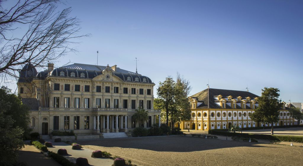 청명한 푸른 하늘 아래 나무로 둘러싸인 탁 트인 마당을 바라보며 화려한 건축물이 있는 역사적인 건물 두 채가 서 있습니다.