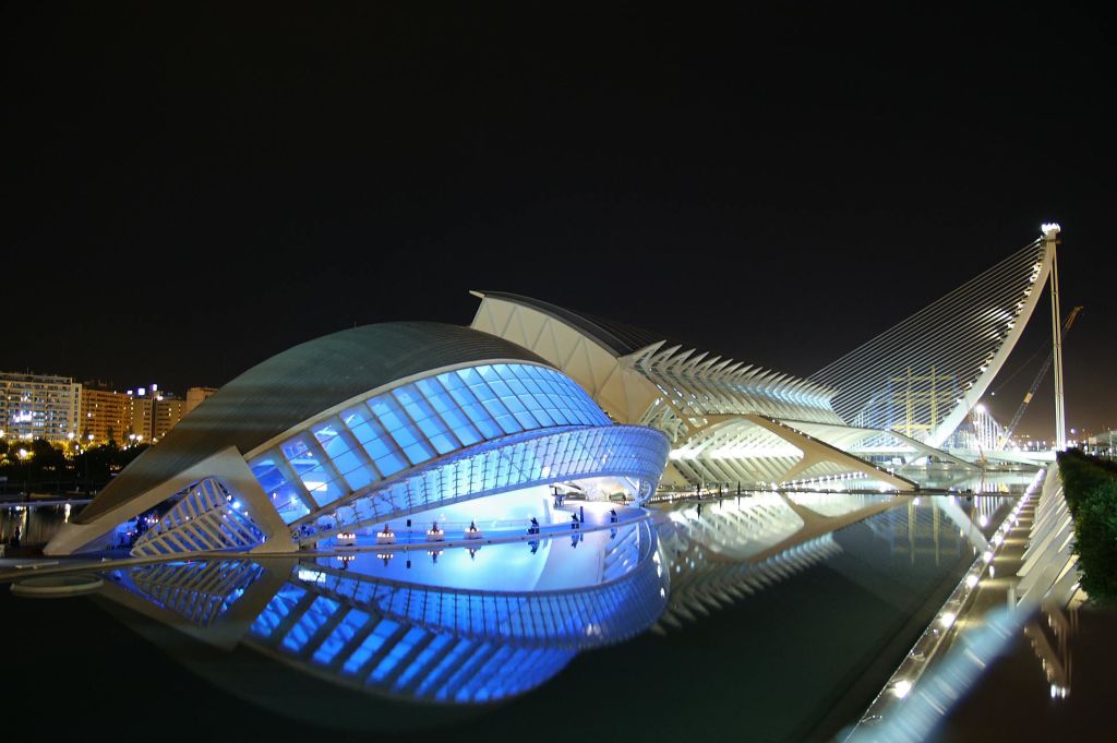 곡선형의 미래 지향적인 디자인이 돋보이는 현대적이고 조명이 있는 건축물은 어두운 밤하늘을 배경으로 잔잔한 물줄기에 반영되어 있습니다.