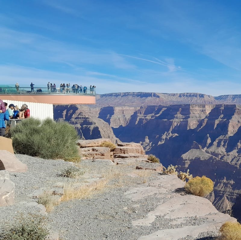 험준한 절벽과 맑고 푸른 하늘을 배경으로 광활한 협곡이 내려다보이는 유리 다리에 사람들이 서 있습니다.