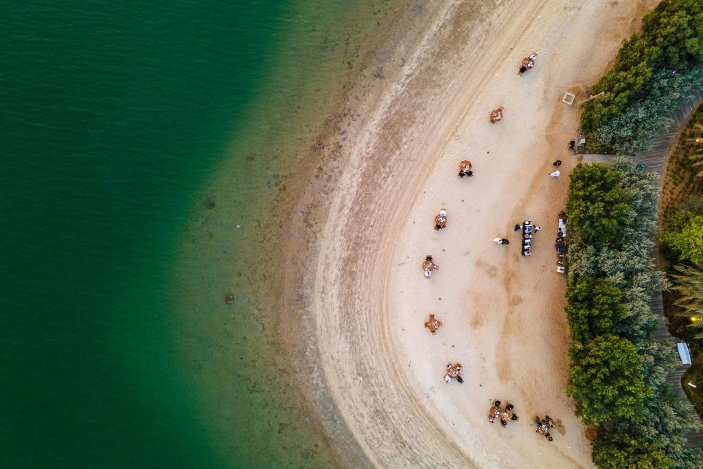 녹지 근처의 탁자에 앉아 맑고 푸른 물과 경계를 이루는 모래 해변의 공중 전망.