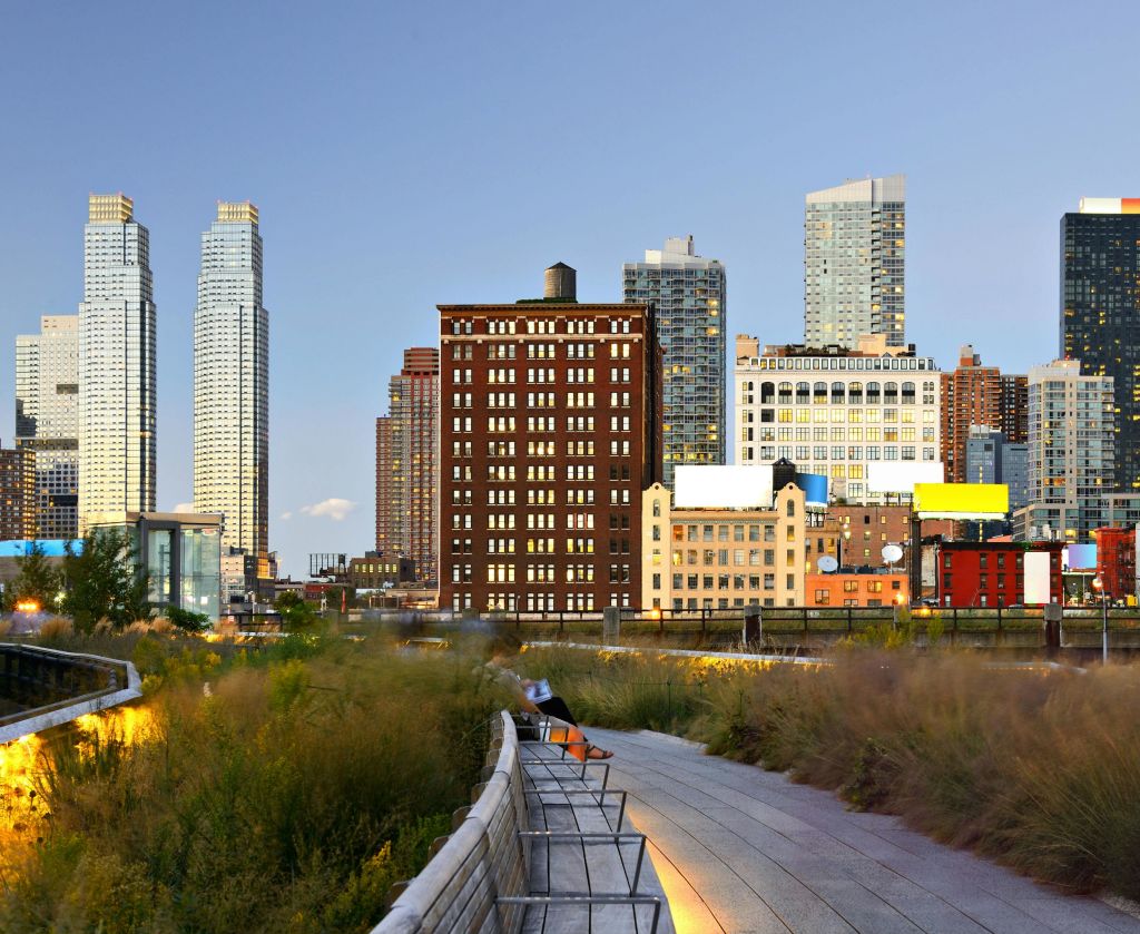 전경에 녹음이 우거진 통로, 해질 무렵을 배경으로 다양한 건물이 있는 도심의 스카이라인.