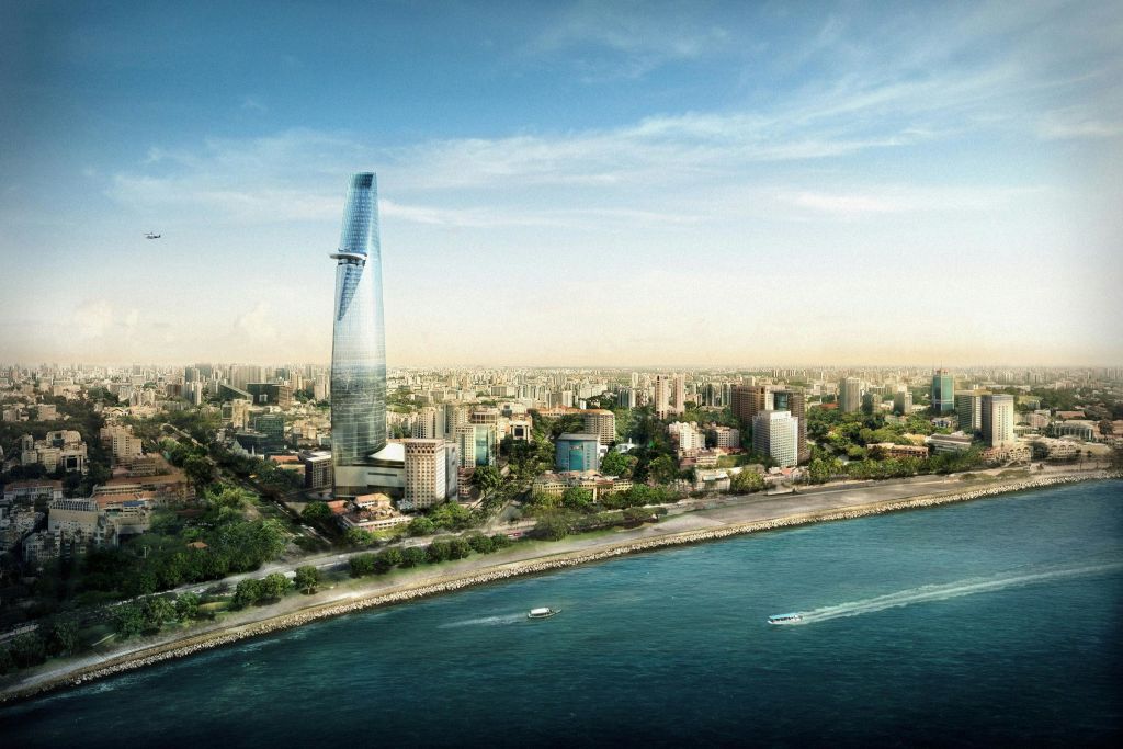 높고 세련된 고층 건물이 해안가 근처의 도시 경관 위로 솟아 있으며, 부분적으로 흐린 하늘 아래 물 위에 두 척의 보트가 있습니다.