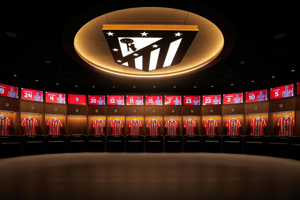 조명이 있는 칸막이 아래에 빨간색과 흰색 줄무늬 유니폼이 배치되어 있고 천장에 로고가 있는 라커룸입니다.