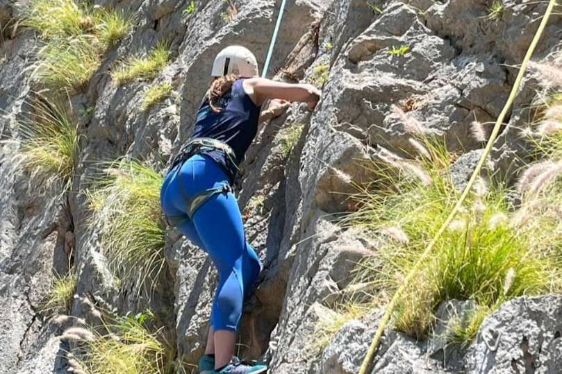 헬멧을 쓰고 등반 장비를 착용한 사람이 잔디 덩어리로 둘러싸인 바위 절벽에 올라갑니다.