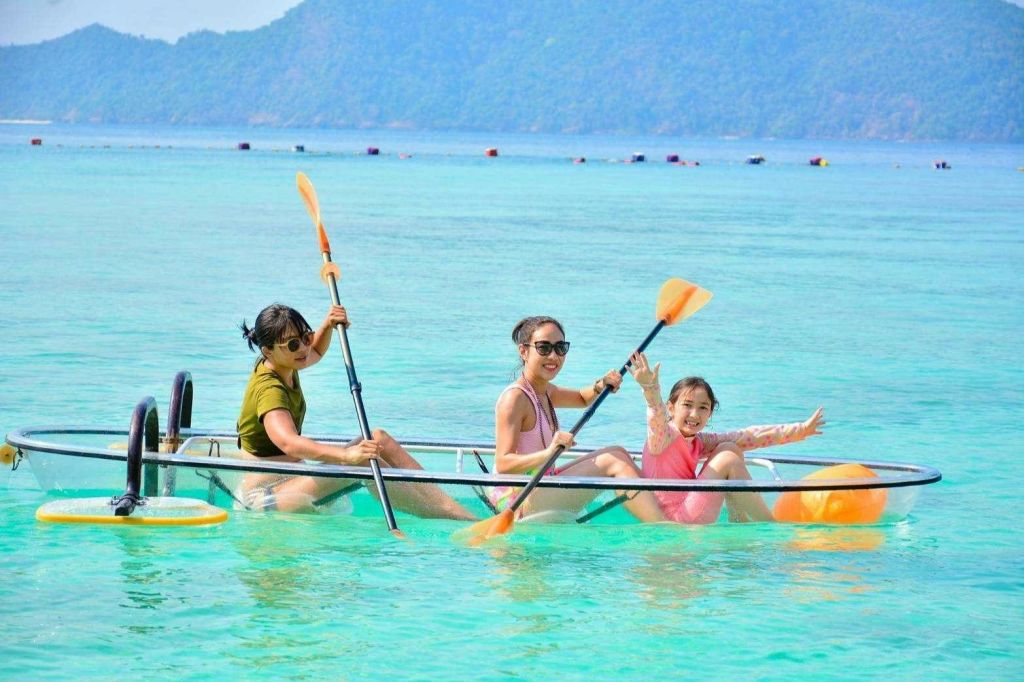 먼 언덕을 배경으로 청록색 바다에서 투명 카약을 타는 두 사람.