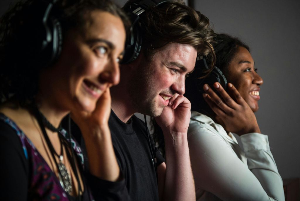세 사람이 나란히 헤드폰을 통해 미소를 짓고 오디오를 듣고 있습니다.