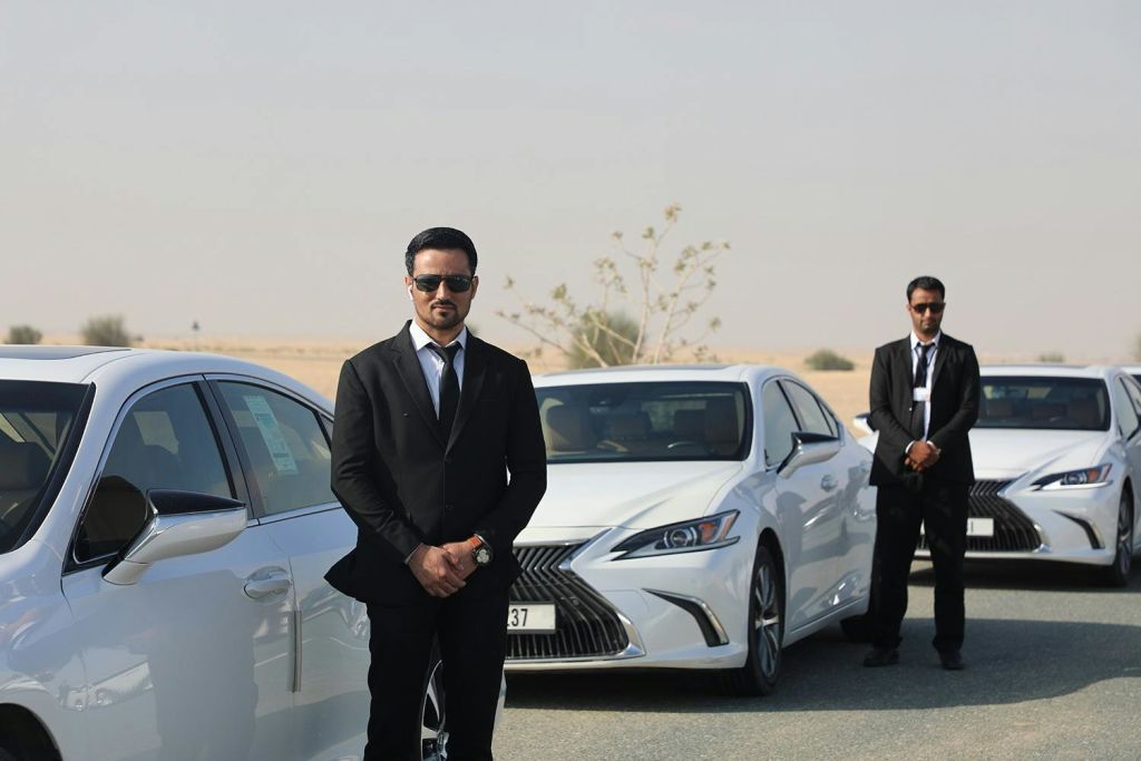 사막 환경에서 두 대의 흰색 자동차 사이에 선글라스를 끼고 검은색 정장을 입은 남성.