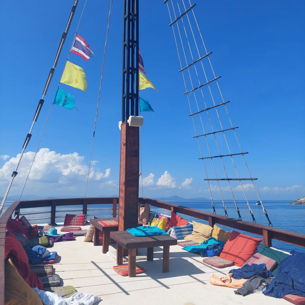 고요한 바닷물에 둘러싸인 맑고 푸른 하늘 아래 화려한 쿠션, 깃발, 벤치가 있는 요트 갑판.