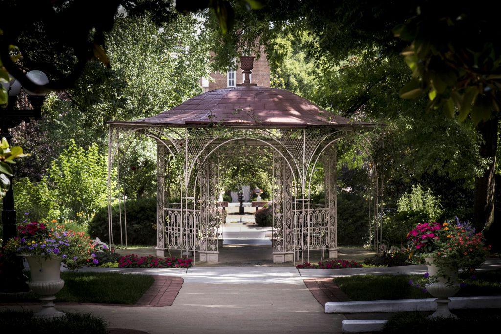 정교한 금속 세공품과 붉은 지붕이 있는 장식용 정자는 울창한 녹음과 화려한 꽃으로 둘러싸여 있습니다.