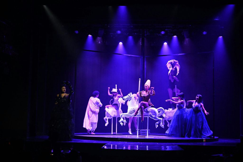 보라색 조명으로 빛나는 회전목마 무대에서 한 사람은 어두운 옷을 입고 다른 사람은 의상을 입고 있습니다.