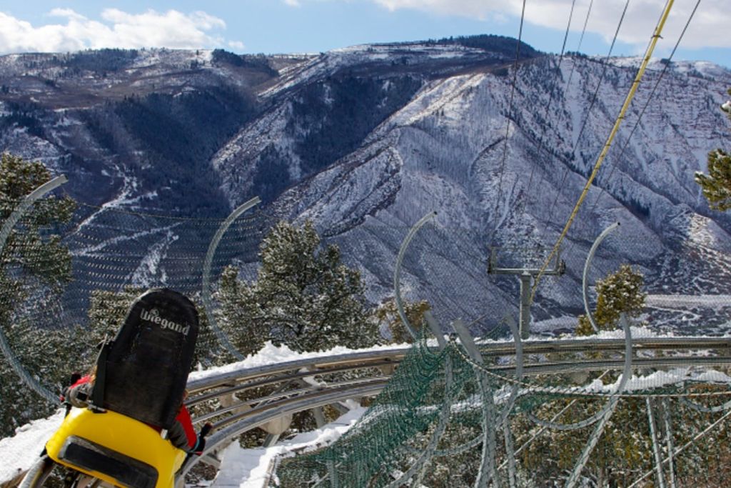 나무와 안전망이 있는 눈 덮인 산 풍경의 롤러코스터 트랙에 있는 썰매.