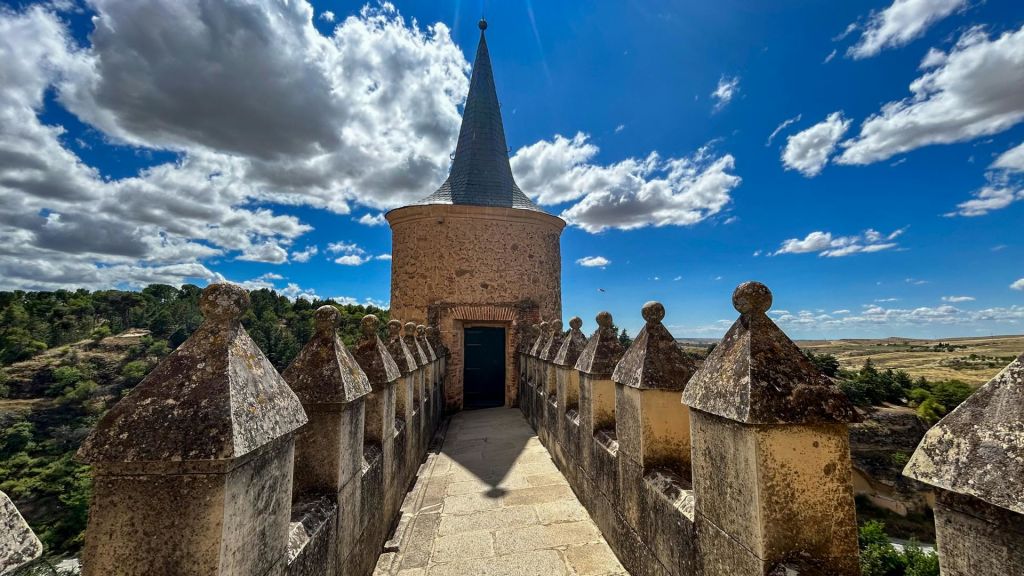 구름이 흩날리는 푸른 하늘 아래 원뿔 모양의 지붕이 있는 원형 타워로 이어지는 돌 통로.