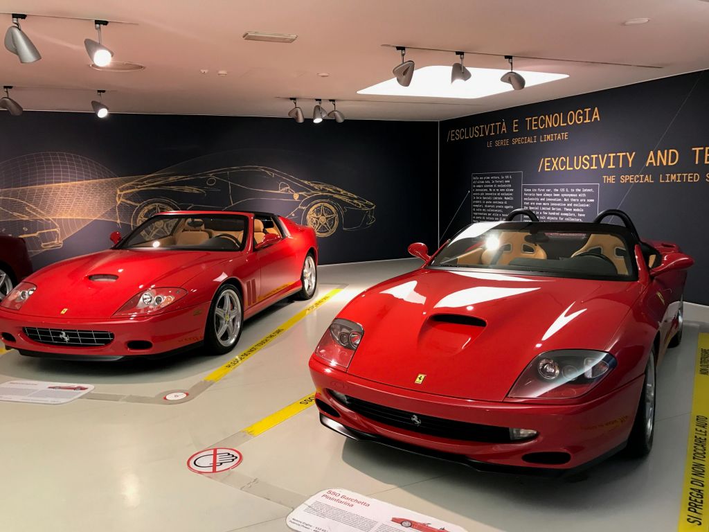 두 개의 빨간색 페라리 컨버터블이 뒤쪽 벽에 정보 패널이 있는 쇼룸에 전시되어 있습니다.