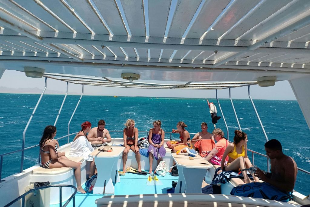 수영복을 입은 한 무리의 사람들이 보트에서 그늘진 캐노피 아래 앉아 담소를 나누고 있으며, 바다를 배경으로 바다가 보입니다.