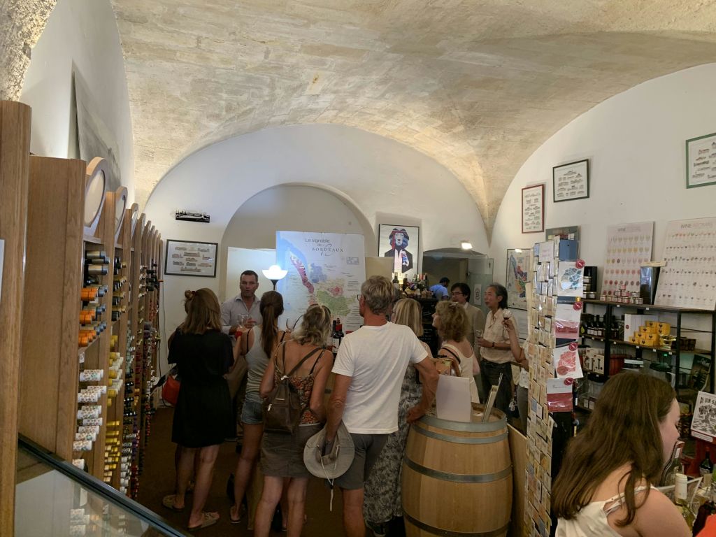 아치형 천장이 있는 와인숍에서 선반과 배럴 테이블 근처에서 와인을 둘러보고 시음하는 사람들.