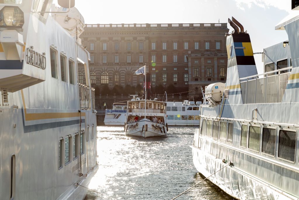 커다란 유서 깊은 건물을 배경으로 물 위의 계류선 두 척 사이를 항해하는 보트.
